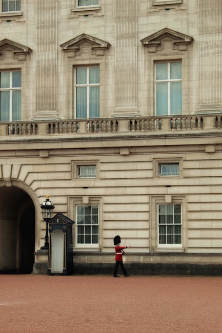 A large, ornate wrought iron gate with black finish and decorative gold accents, set within an arched stone entrance to a historic building. The stone facade around the arch is light-colored and detai